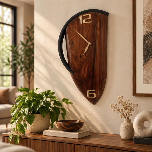 A shield-shaped wooden wall clock with a black curved top trim and gold-tone numerals, displayed on a beige wall above a wooden console table in a styled living room setting.