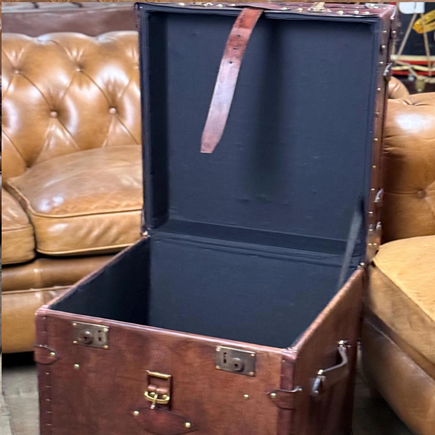 Open brown leather trunk with blue interior against a brown leather couch background