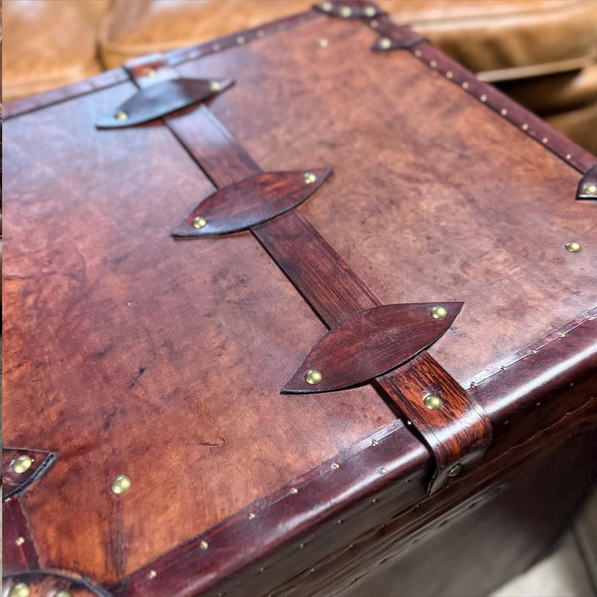 Close-up of a brown leather suitcase with decorative straps and gold rivets.