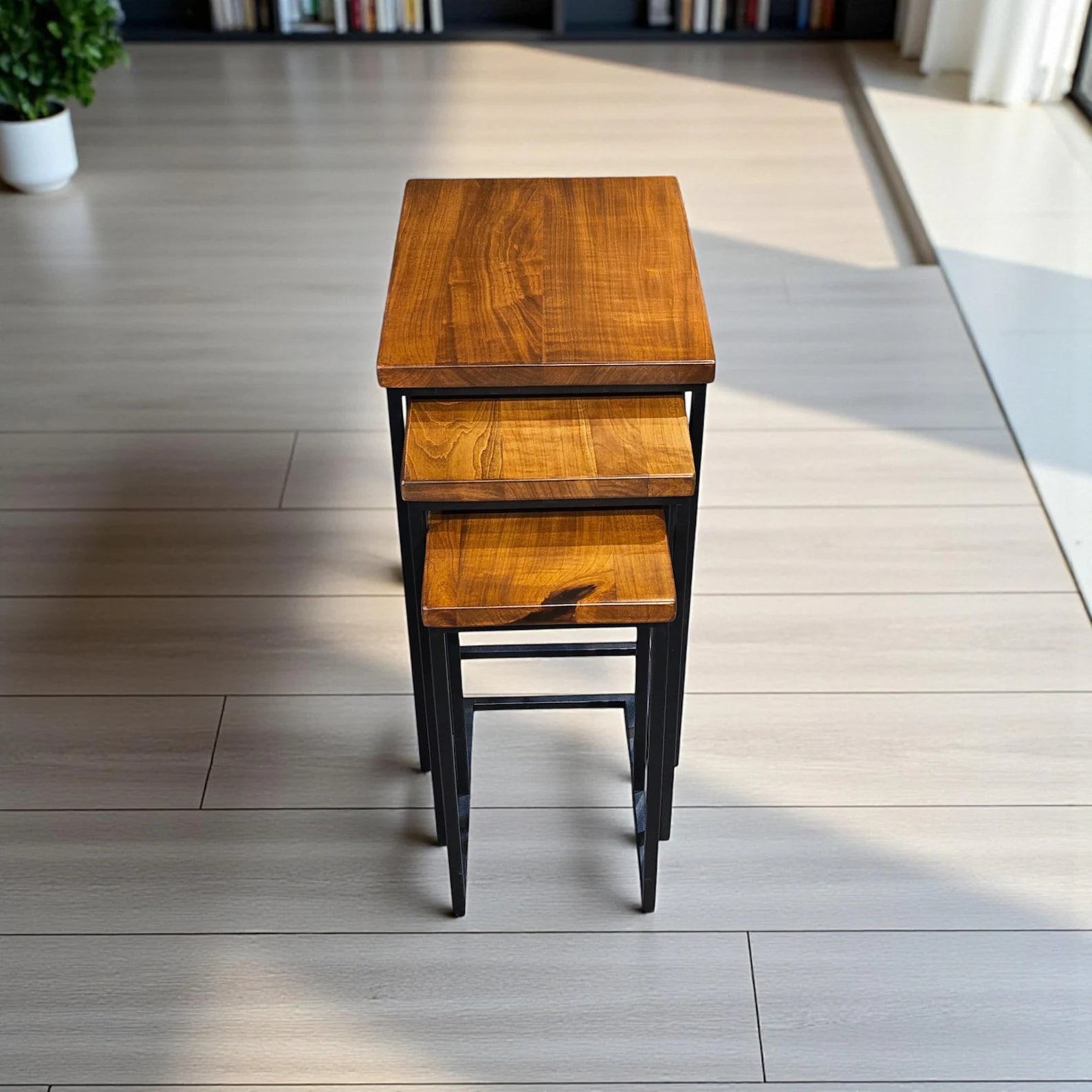 Set of three wooden nesting tables with black metal legs in a room setting.