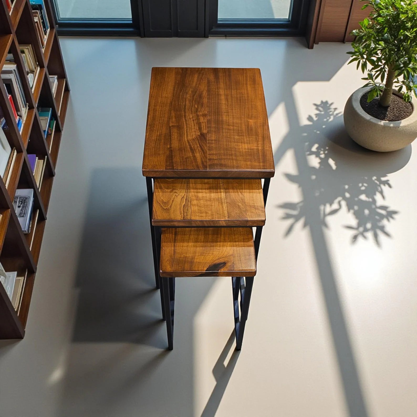 Set of three wooden nesting tables with black metal legs in a room setting.