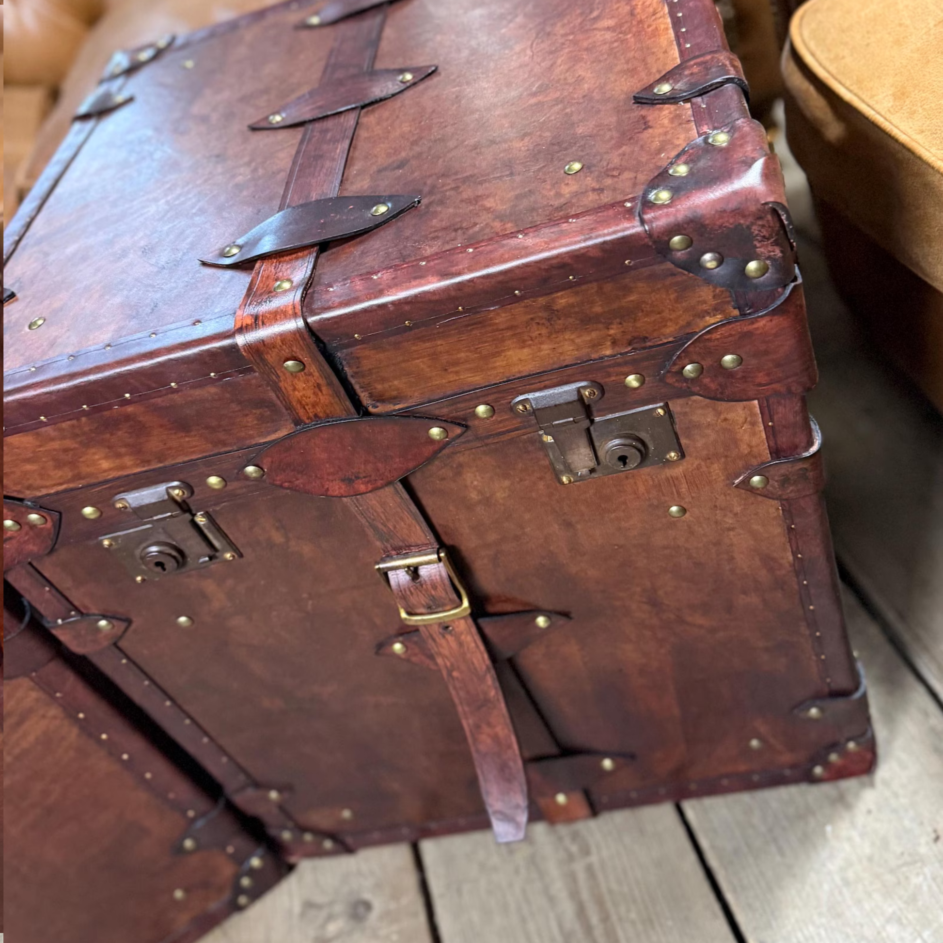Vintage brown leather trunk with brass studs and buckles on a wooden floor.