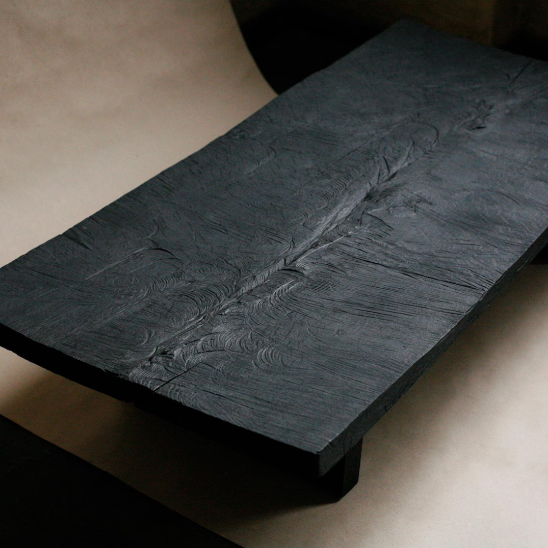 A rectangular black wooden board or tray with a thick, textured top surface showing natural wood grain and a prominent central crack, photographed on a neutral beige background.