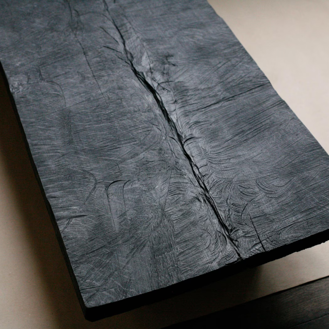 A close-up of a dark charcoal gray textured board with a prominent vertical crack and swirling grain patterns, resting on a neutral beige surface.