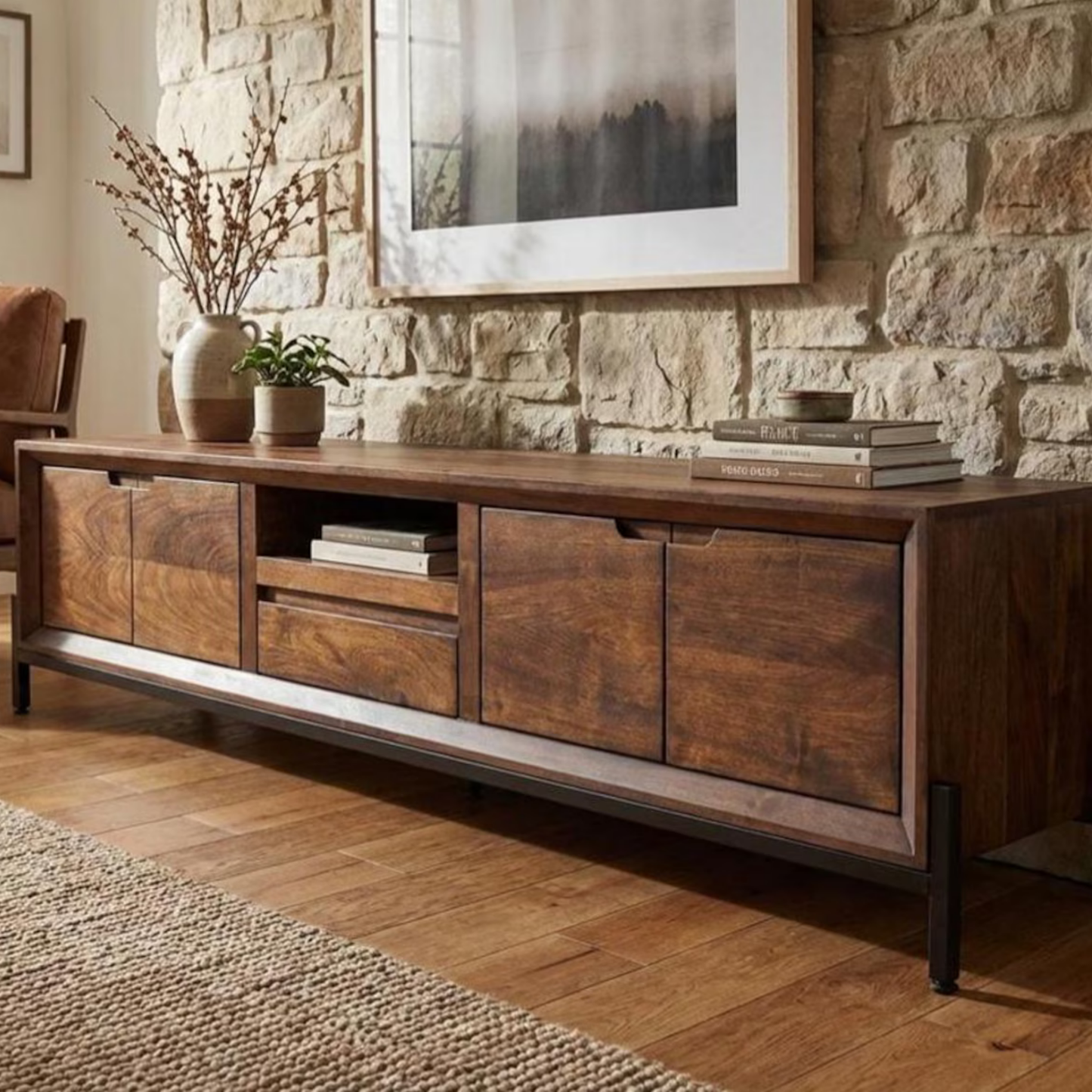 Wooden entertainment console in a living room with stone wall and framed picture.
