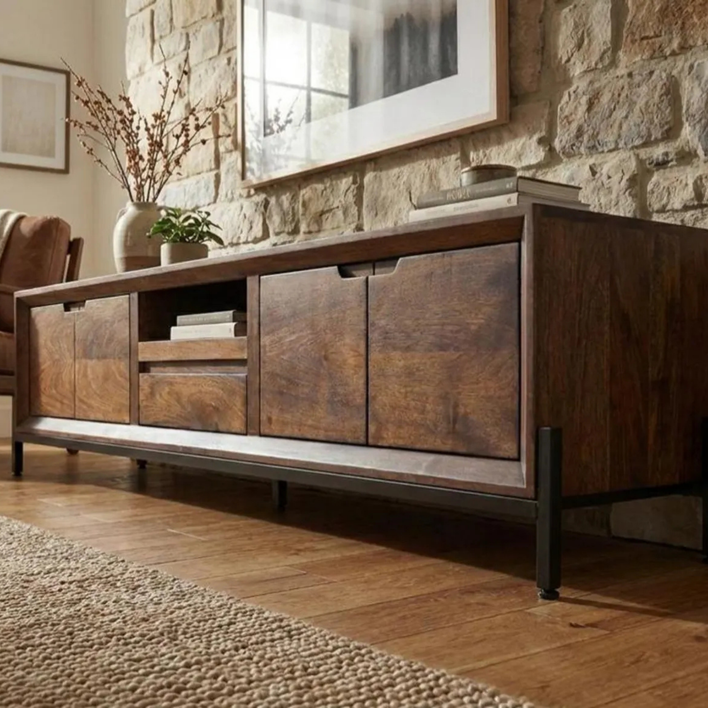 Wooden entertainment console in a living room with stone wall and decor.