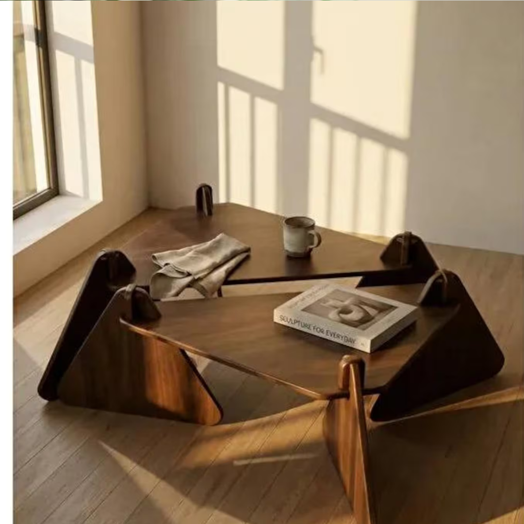 A modern low wooden table with sculptural angular legs, styled in a sunlit room with a mug, folded cloth, and book on top.