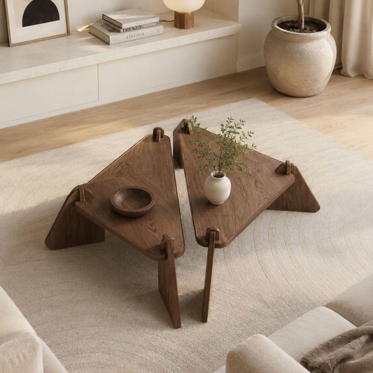 A modern two-piece wooden coffee table set in a bright, contemporary living room. The set consists of two triangular wooden tables with a rich walnut-like brown finish, connected by a small wooden bowl in the center.
