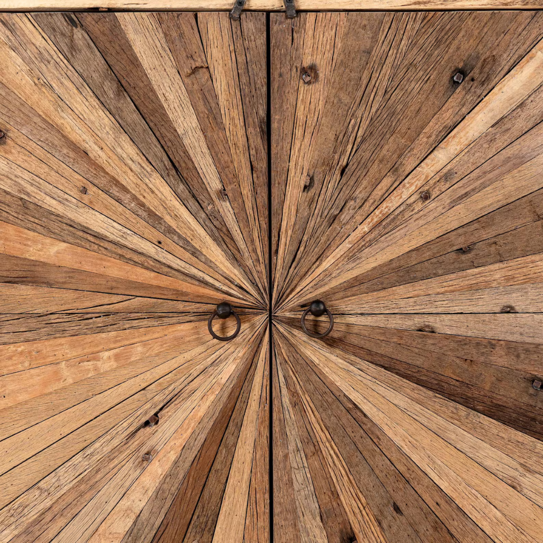 Close-up of a rustic wooden cabinet door with a radial starburst pattern made from radiating wood planks, featuring two black metal ring pulls at the center.