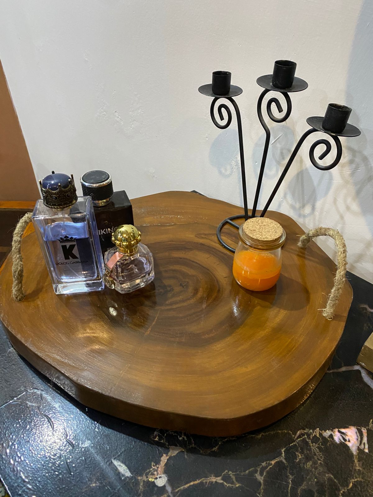Wooden tray with decorative items including a candle holder, small bottles, and a jar on a marble surface.